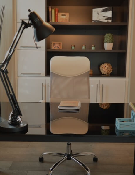 A home study with a mesh desk chair, an angled desk lamp and books on built-in shelving.